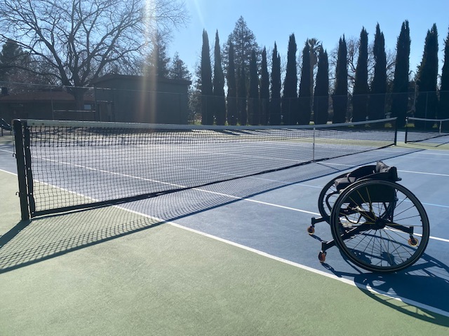empty wheelchair sitting on tennis court by the net